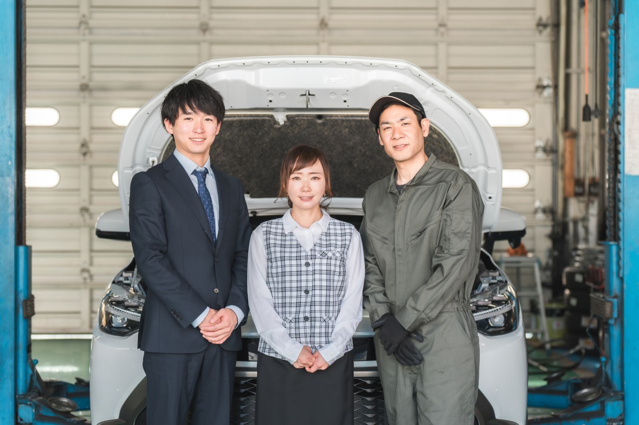整備工場内で笑顔で並ぶ3名のスタッフ