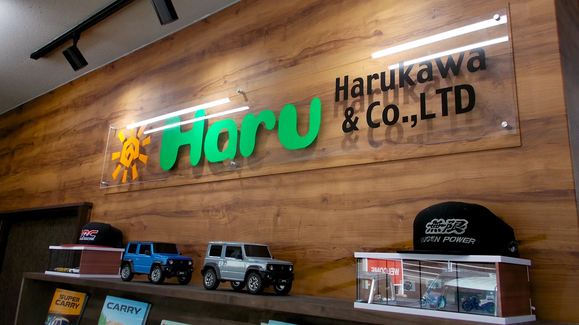 木目調の壁に掲げられた「Haru Harukawa & Co., LTD」の店舗ロゴと、ジムニーのミニカーなどが飾られたディスプレイ