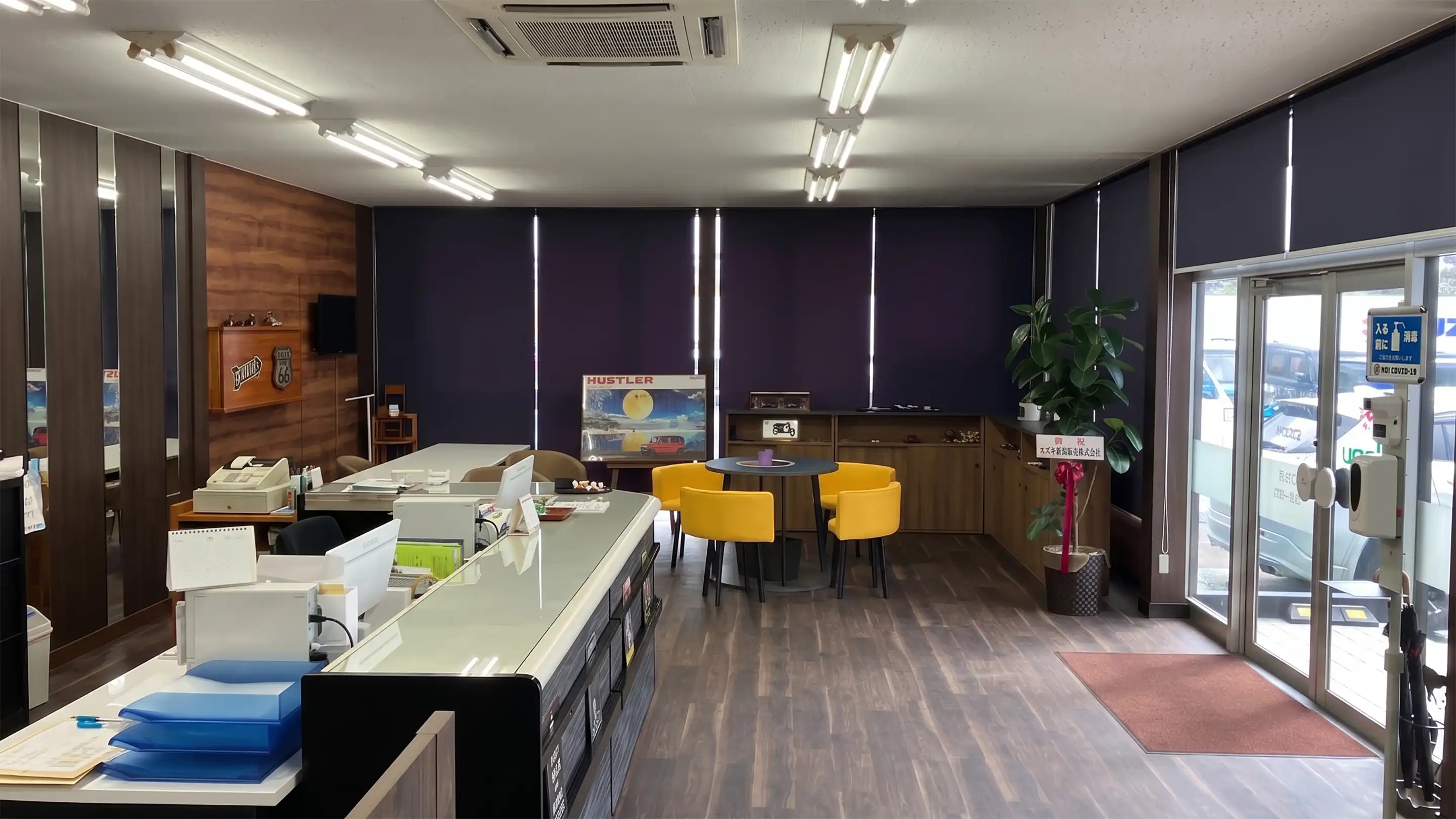 店舗入り口の様子。右手にガラス張りの入り口、左手に受付カウンター、中央に黄色いチェアが配置された商談用丸テーブルがある、清潔感のある空間